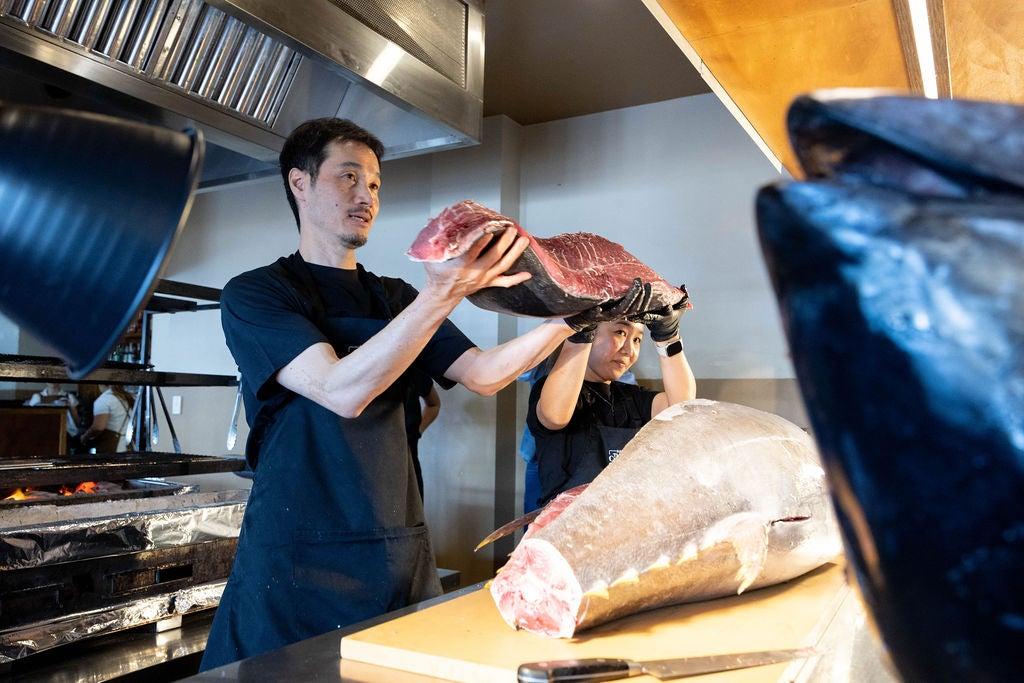 Chef from SOKA Restaurant holding up a piece of sliced tuna, with the main tuna body still on the table.