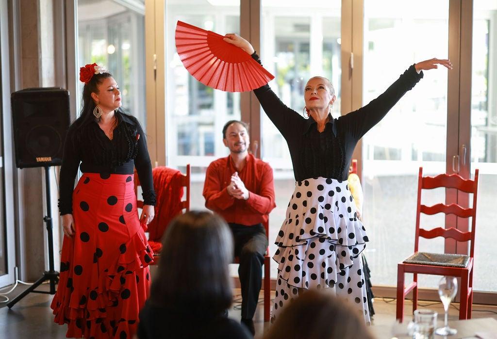 Three Spanish performers - one holding a red fan arms out wide in a dance