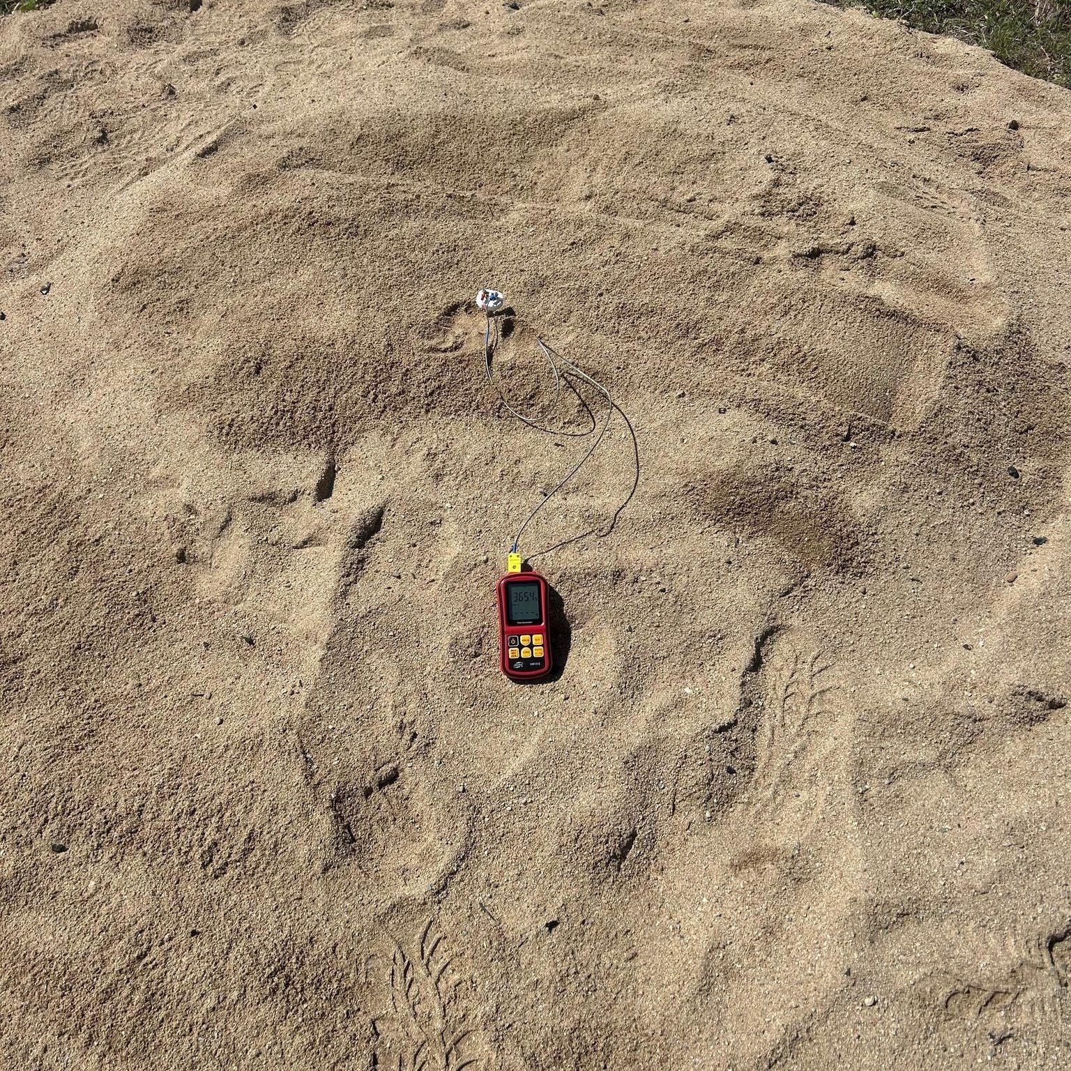 pit dug onto beach showing a temperature gauge in the centre