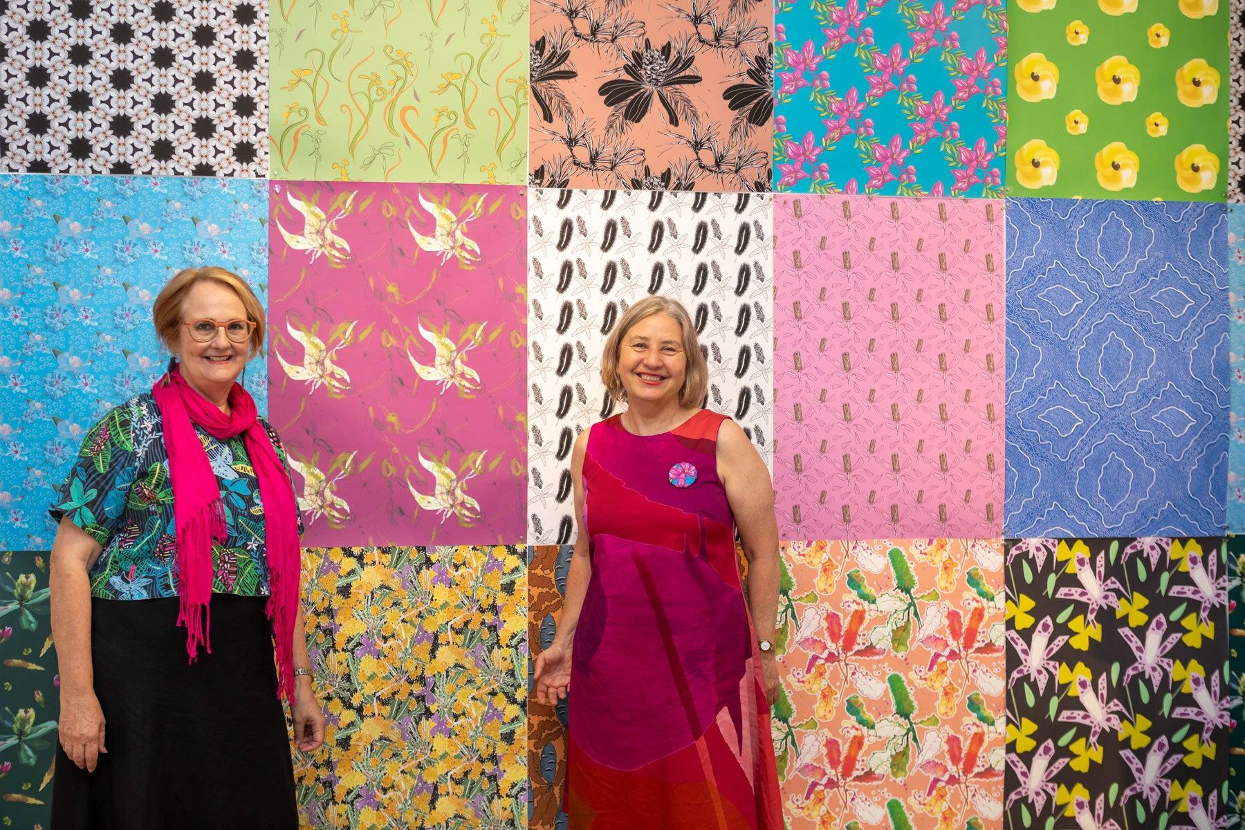 Two women standing in front of an artwork at the Wildflowering by Design exhibition launch