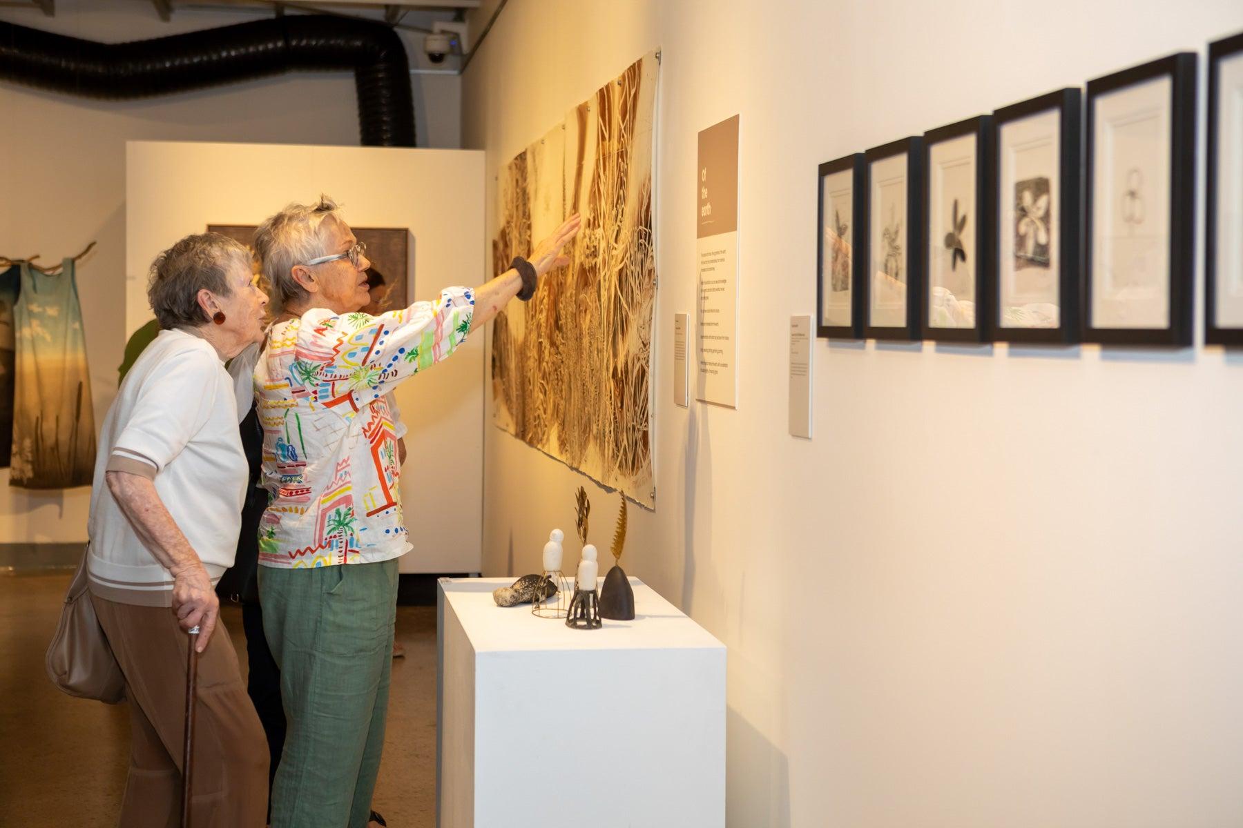 Two women discussing an artwork at the Wildflowering by Design exhibition launch