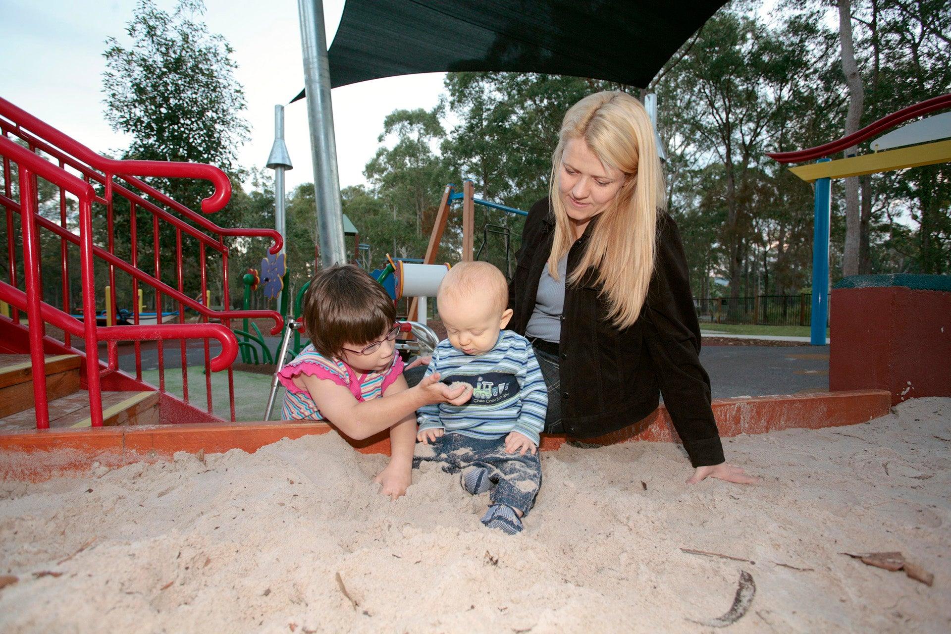Mum with her two children playing in the sand at a playground