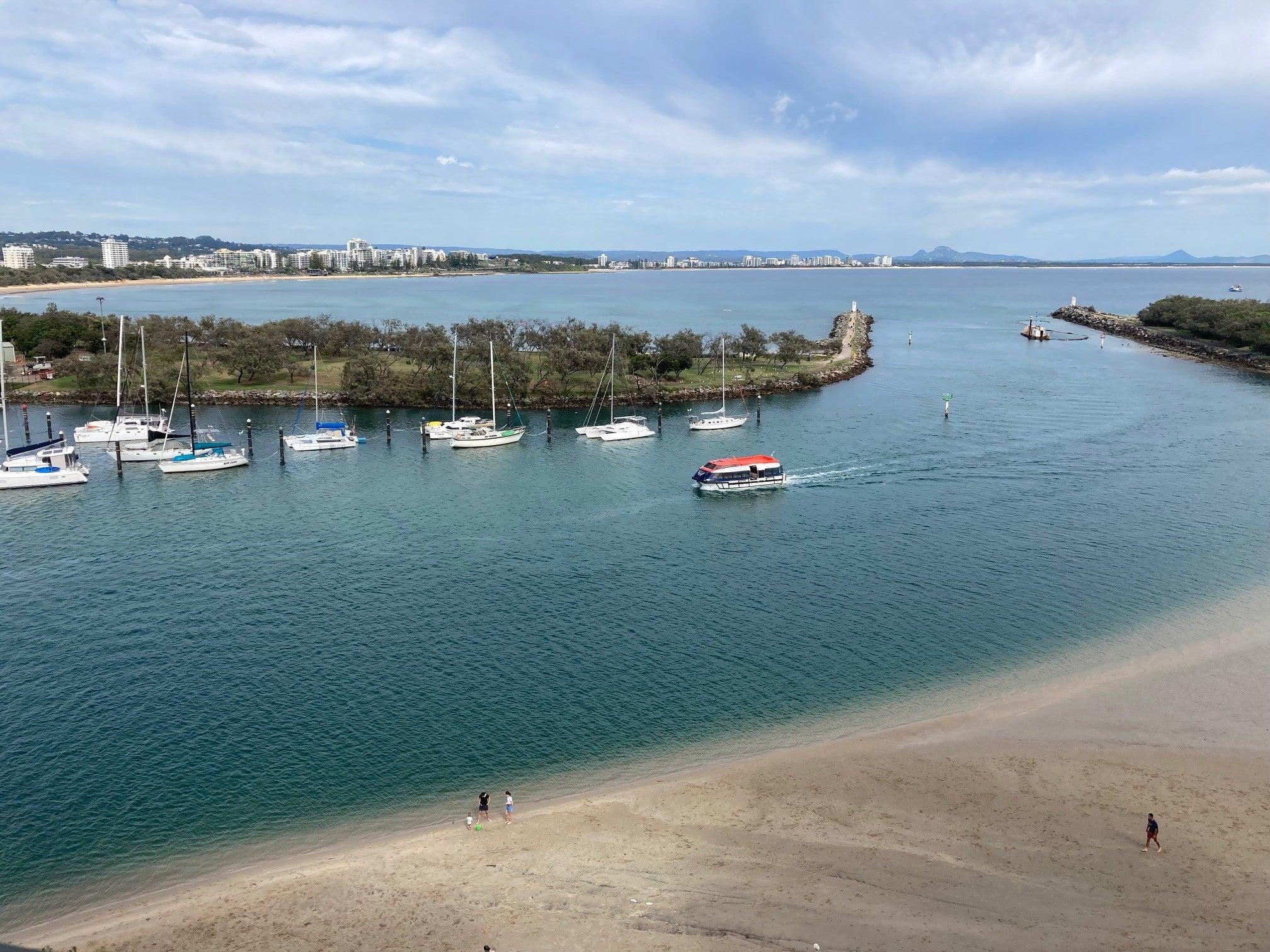 Boat coming into a calm waterway inlet with blue skies and fluffy white clouds. Above shot overlooking a sandy brown beach.