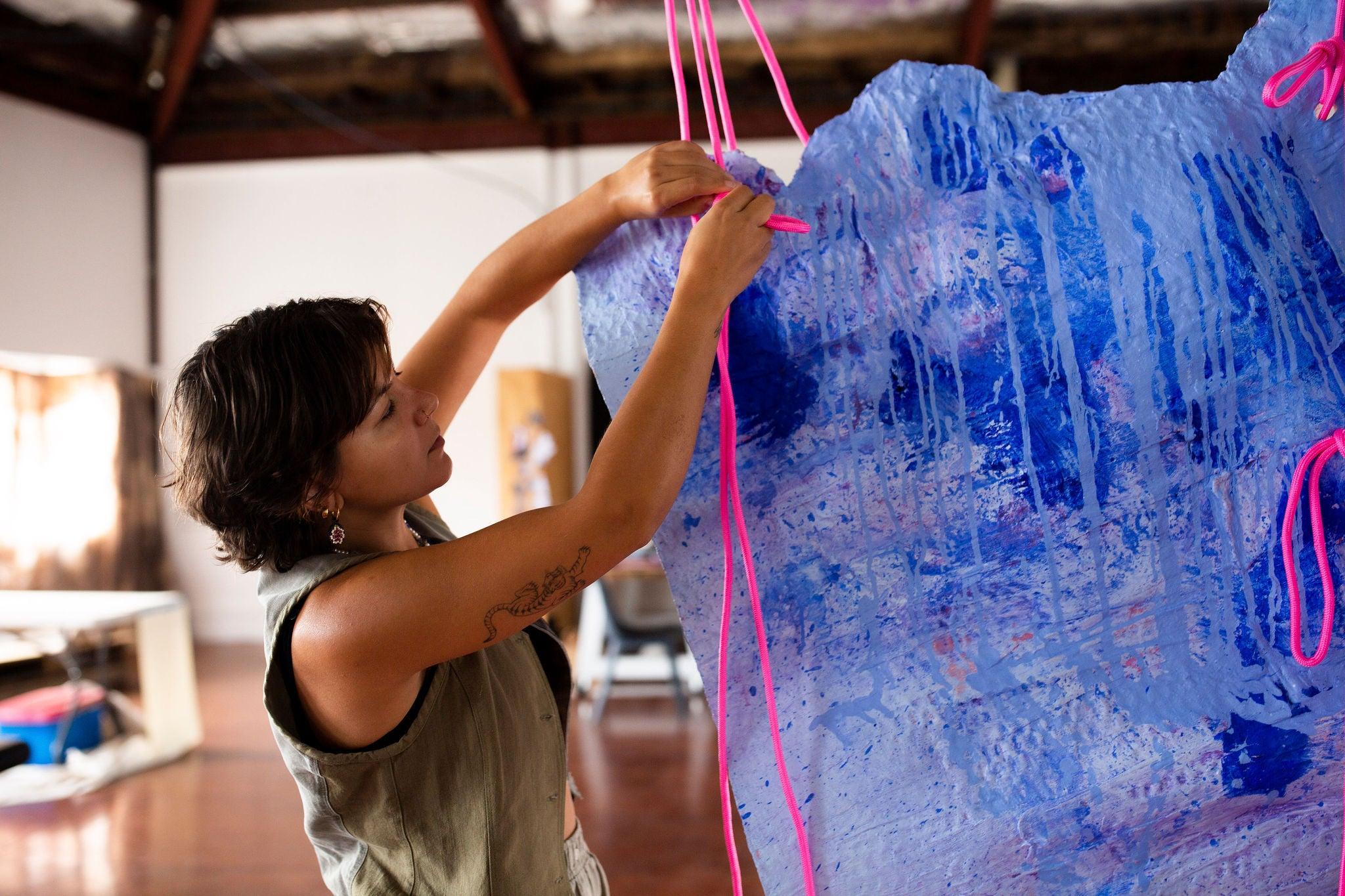 A female artist threading pink cord into a blue artwork