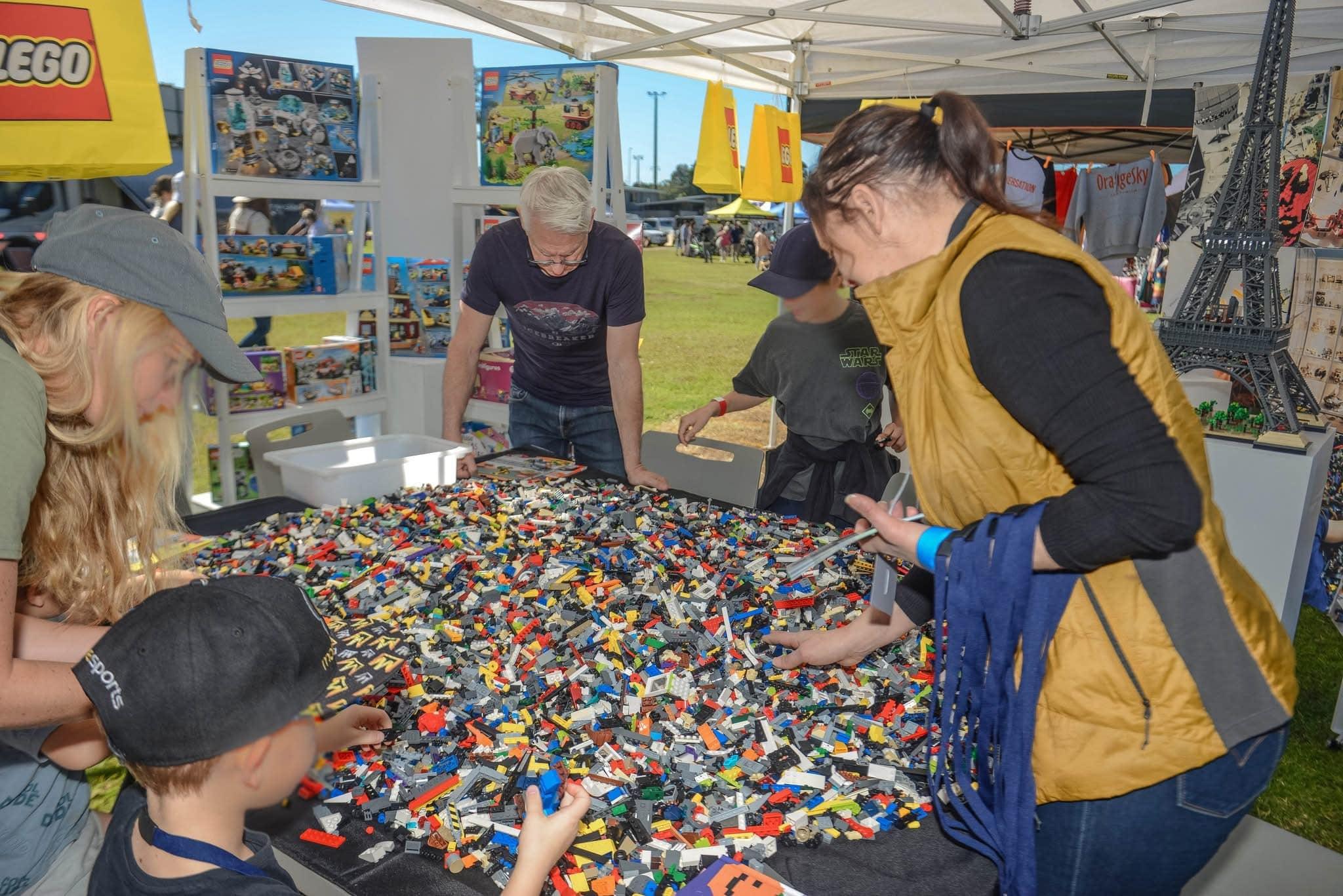 5 people (kids and adults) huddled over a huge table of lego pieces.