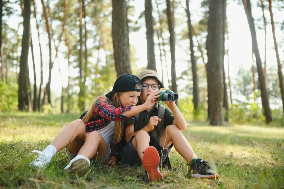 two children sitting outdoors using binoculars