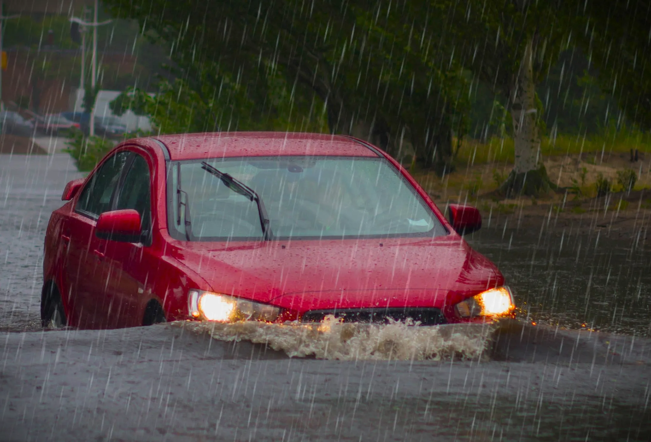 A red car is immersed in flood water that is covering a suburban road.