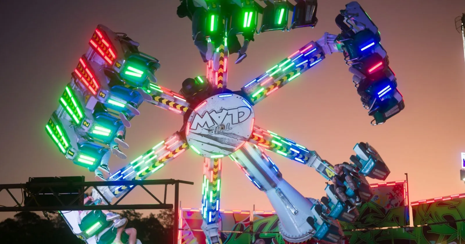 A ride - The Claw all lit up with green, red and blue (purple) lights as it moves through the air.
