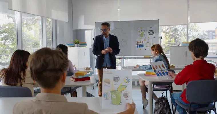 Classroom setting with teacher at the front of class with a large white board behind him teaching students about recycling.
