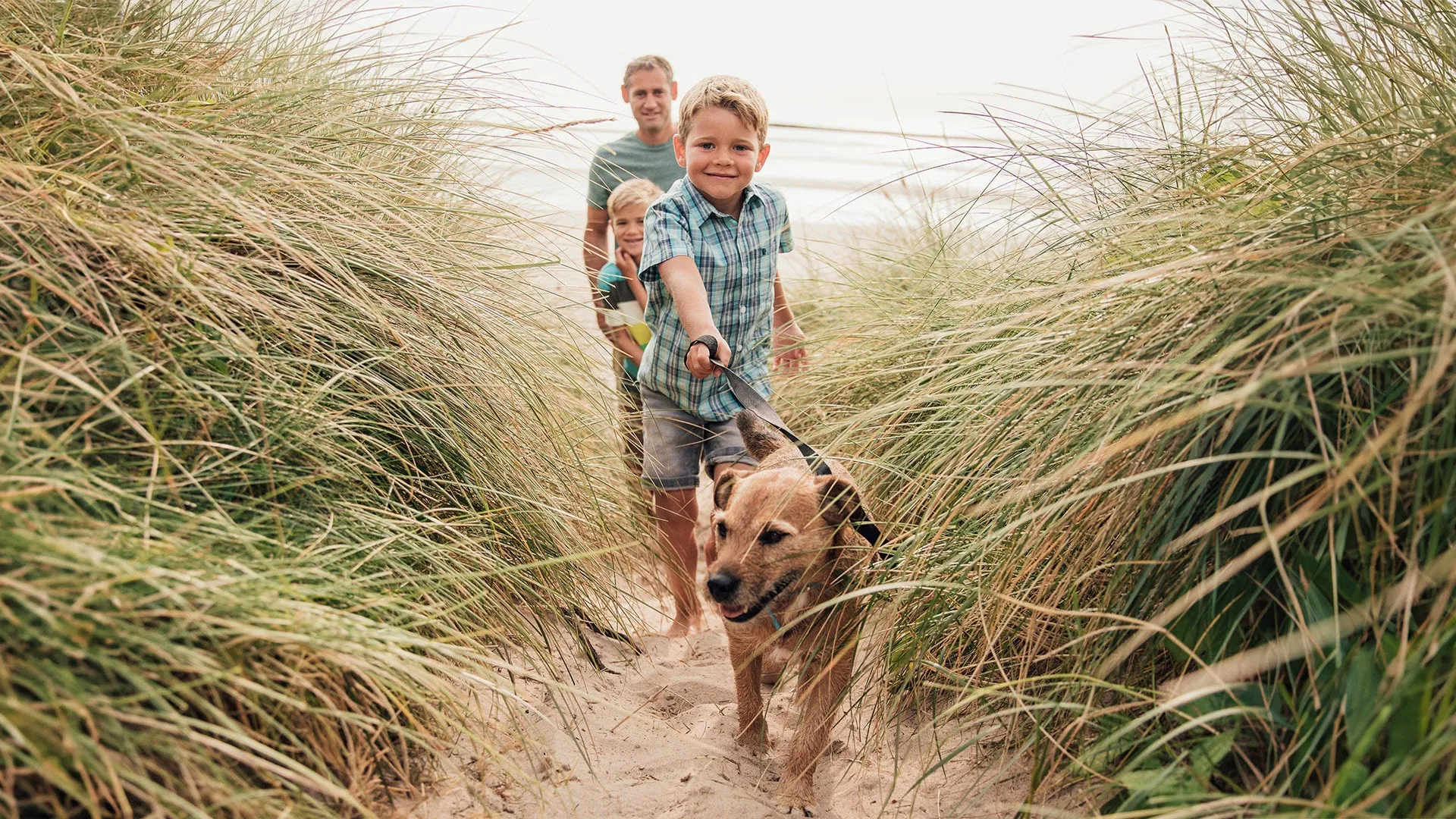 Family of three exiting the beach with a dog on a lead.