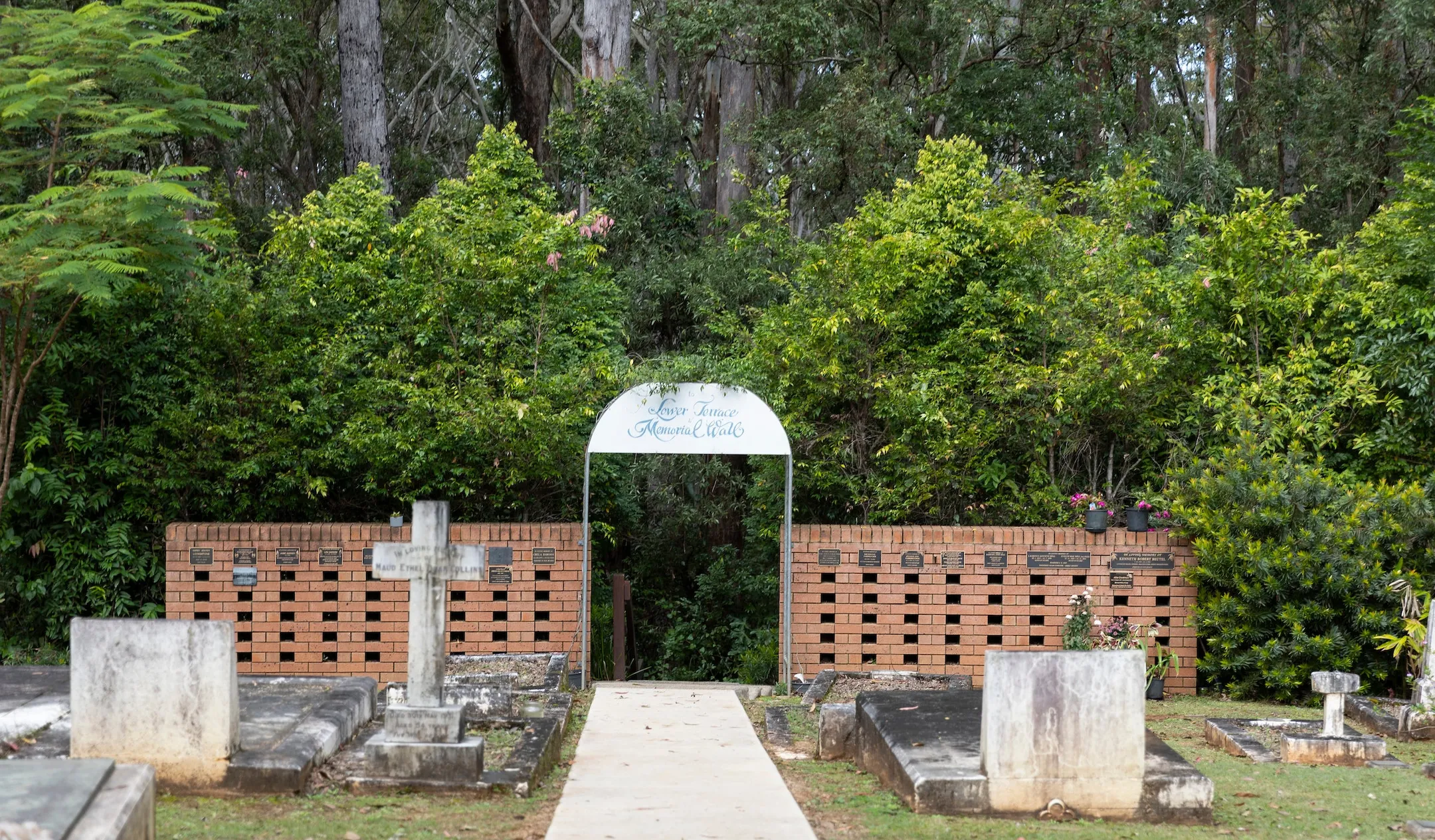 A concrete pathway leads through the centre of the burial section to an arched walkway in the brick niche wall with the dense gardens and bushland beyond.