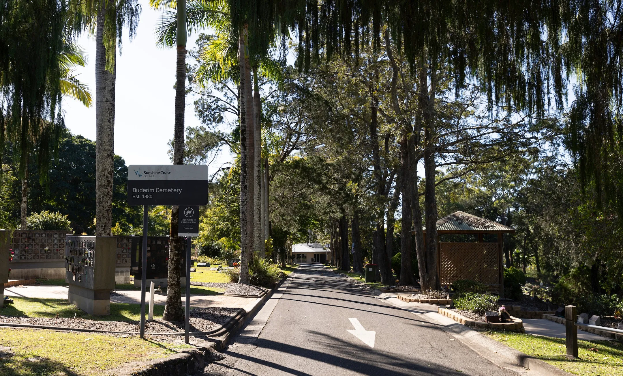 Buderim Cemetery Est. 1880 sign, wall niche on left hand side of image, the exit driveway lined with trees and garden site.