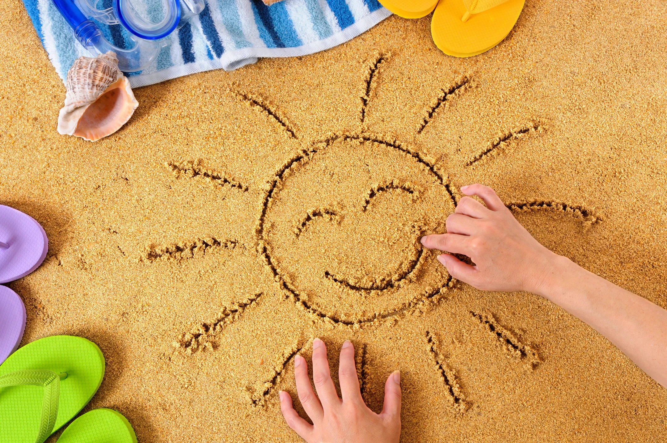 Summer School Holiday Guide picture of child hands drawing the sun in the sand.