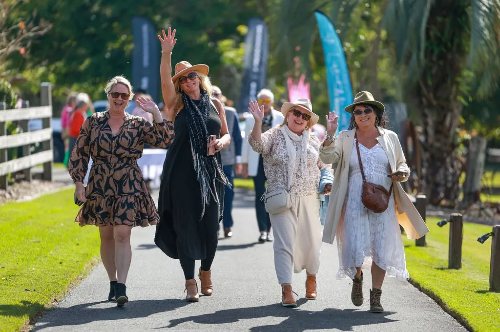 Four ladies walking towards the camera looking happy and hands in the air to save hello