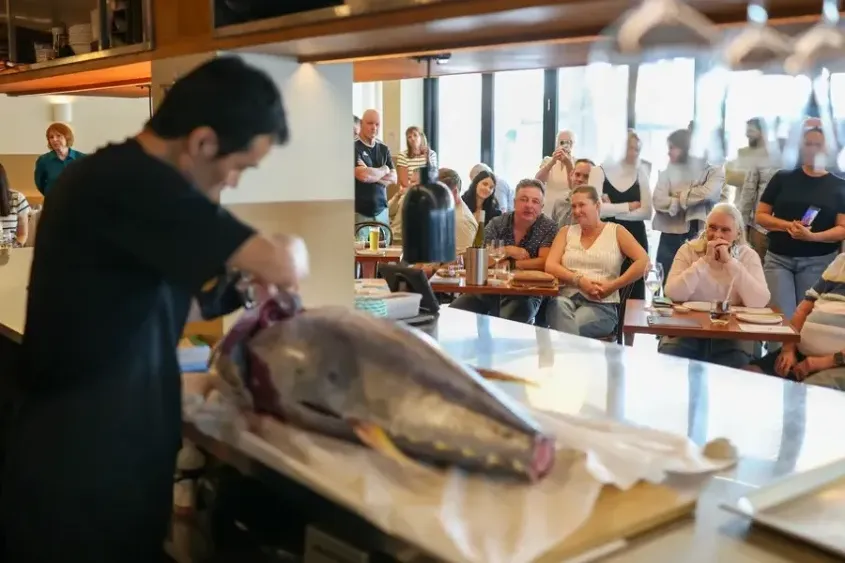 A chef cutting into a tuna fish with people watching on in the background
