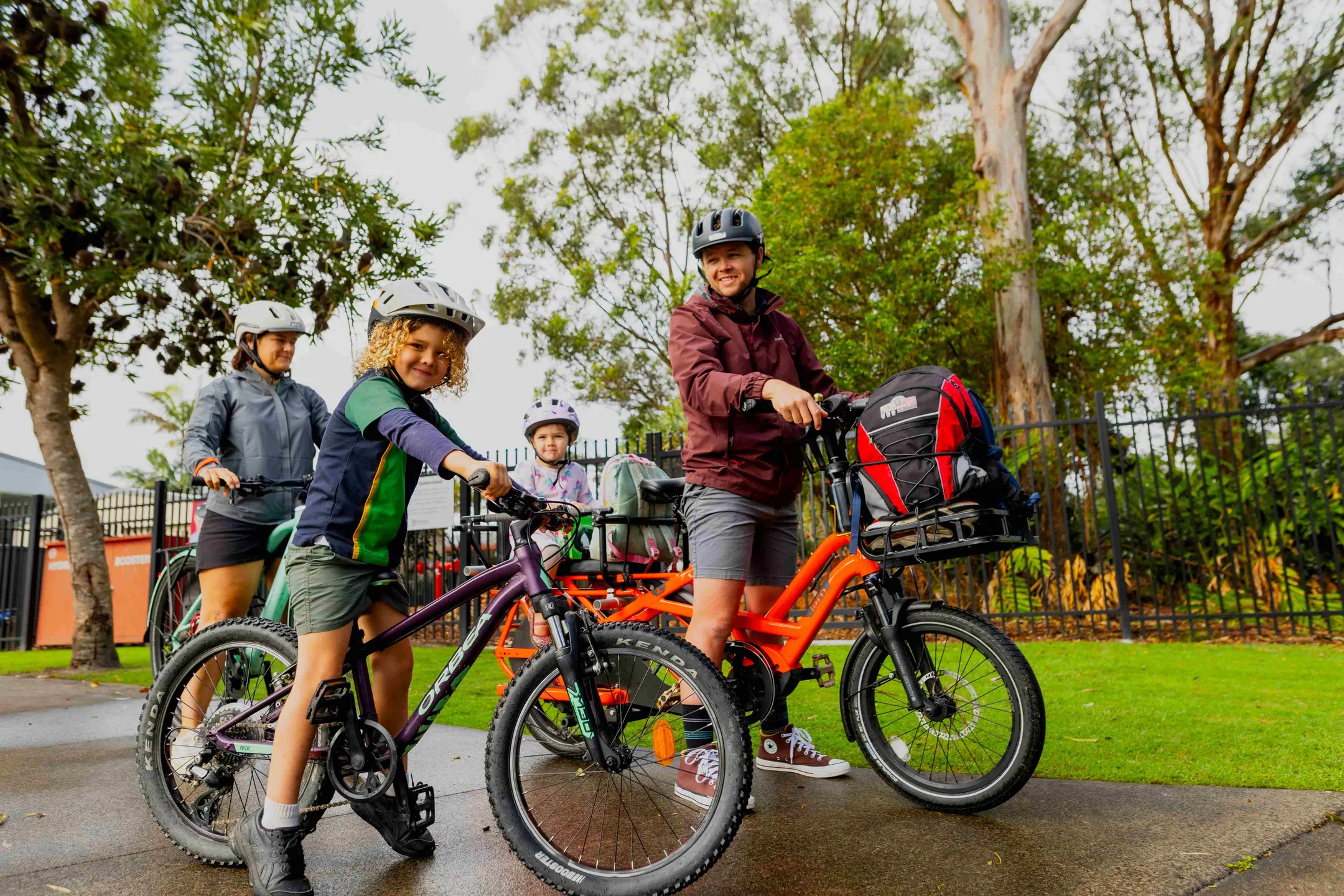 A schoolboy with his mum, dad and little sister are all stationary on bicycles, all wearing helmets.