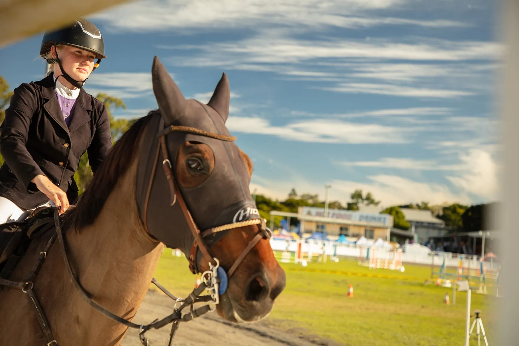 Young person in dressage attire sitting on a horse, with the background of the Nambour Showgrounds - the arena or showring.