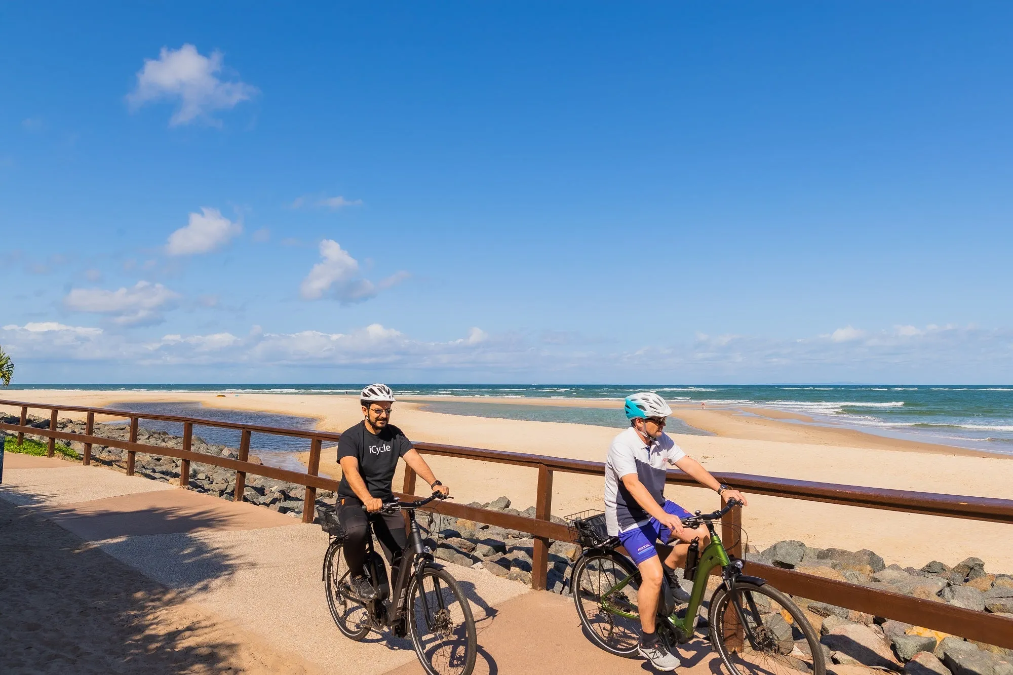 Two people riding electric bikes along pathway near the ocean.