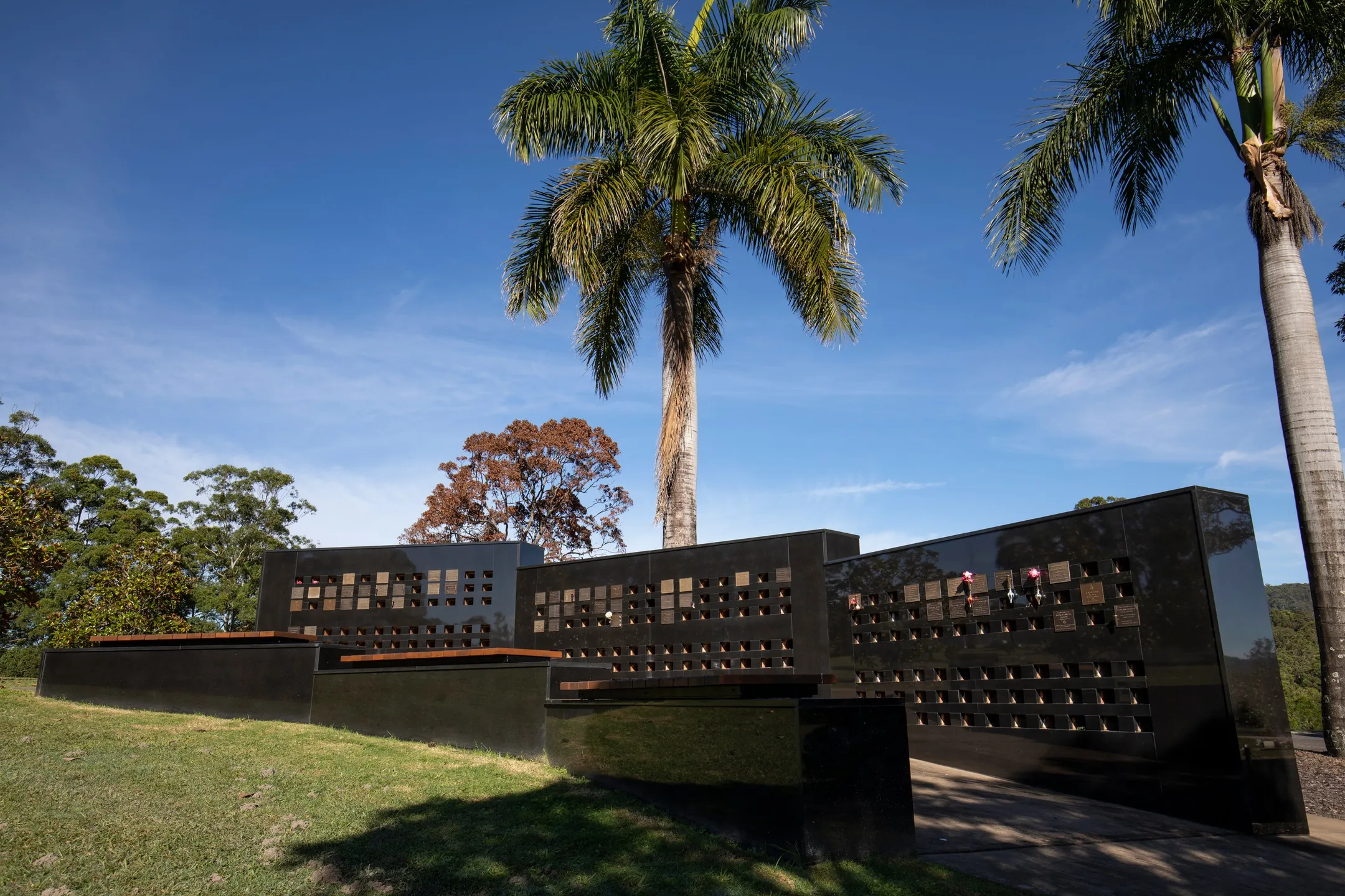Timber seating in front of black stone wall niche, some with bronze memorial plaques.