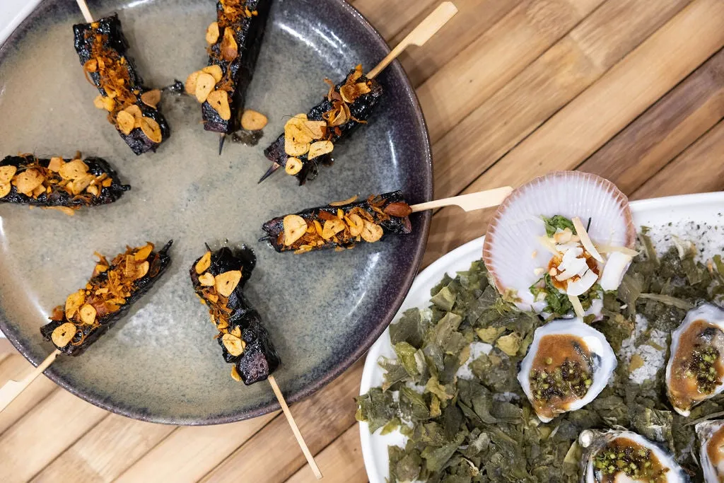 A plate of BBQ skewers and a plate of oysters.