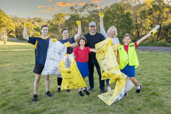Group of six adults and children with large plastic bags celebrating cleaning up a area beside a country road.