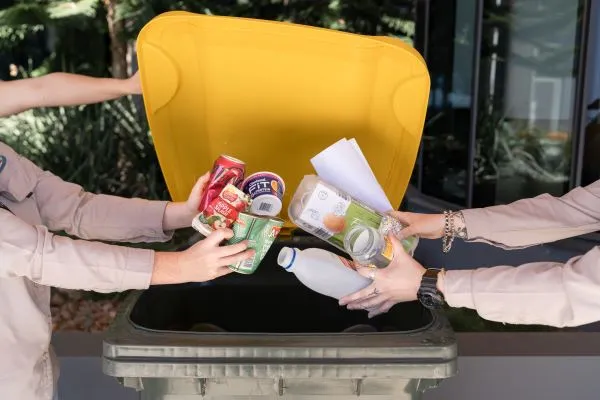 People placing empty recyclable containers into a recycling bin.