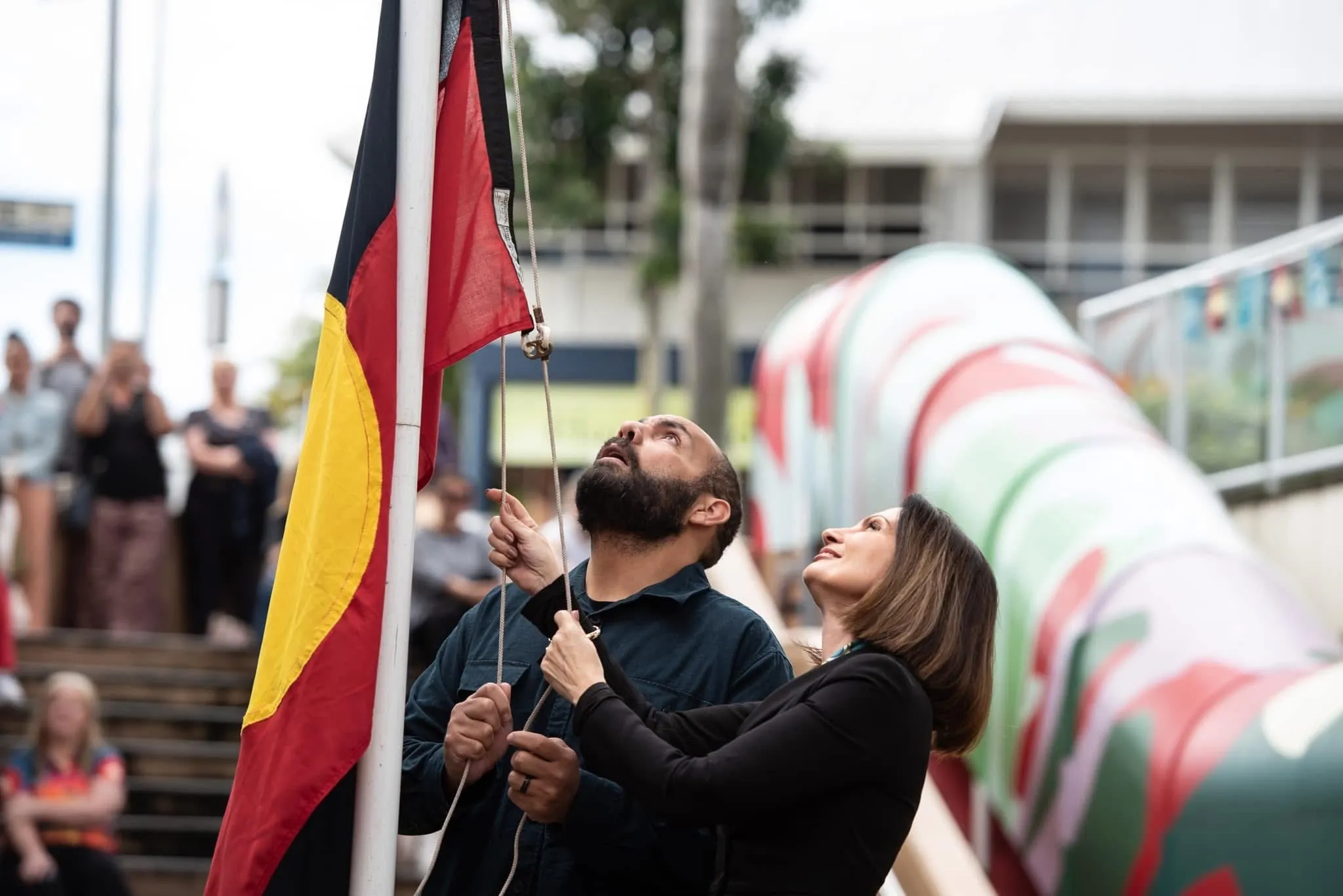 Kabi Kabi man Daniel Neill and Sunshine Coast Council Mayor Rosanna Natoli raise the Aboriginal flag at a NAIDOC Day ceremony in Nambour.