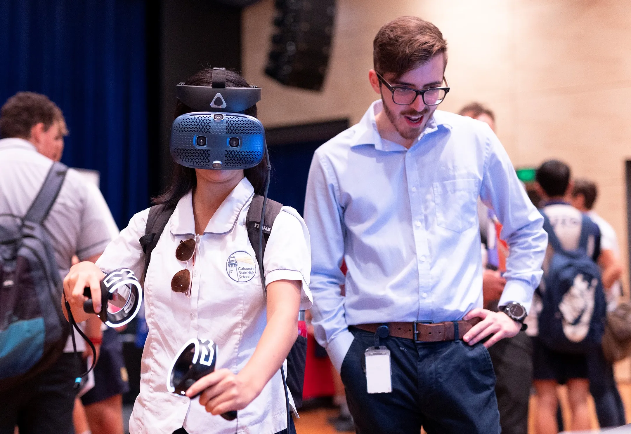 A student trying out tech gear - virtual reality googles and gloves, with a supplier standing beside watching a monitor.