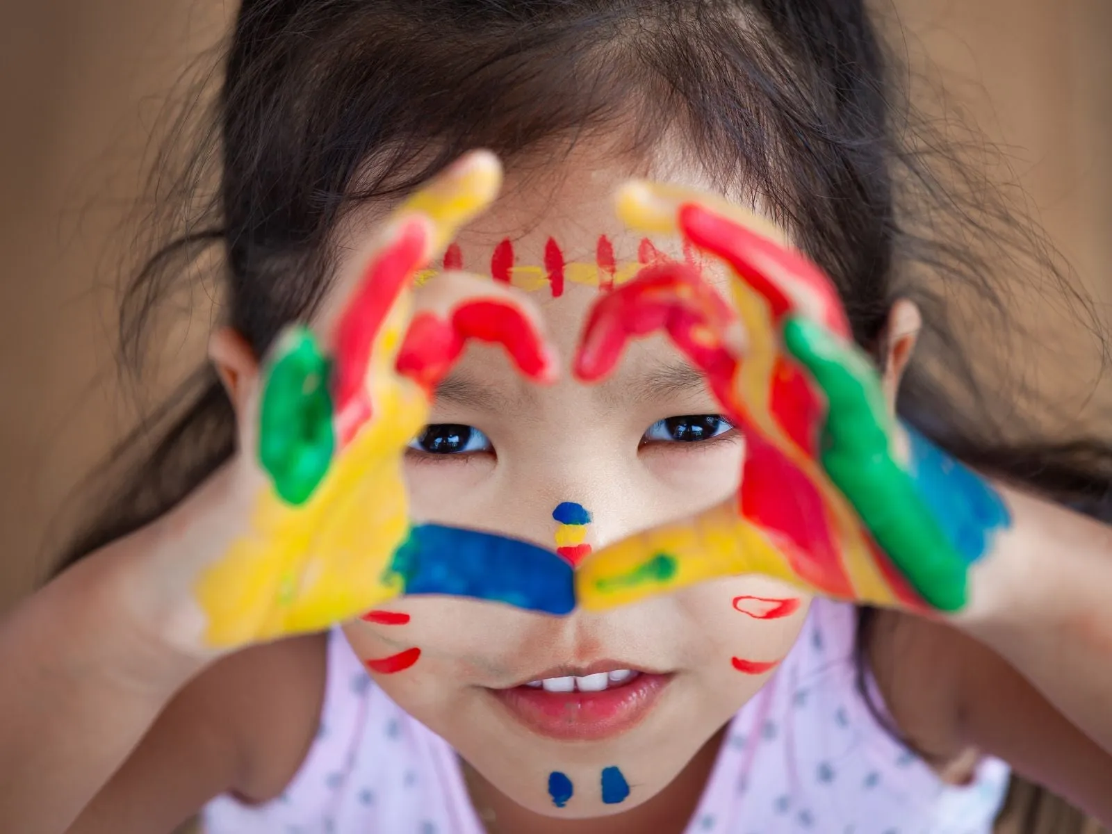 Young girl with colourful paint on her hands making a shape of a heart with her hands.