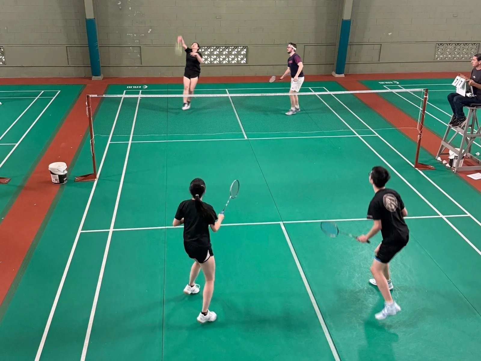 Two men and two women are playing badminton on a green court.