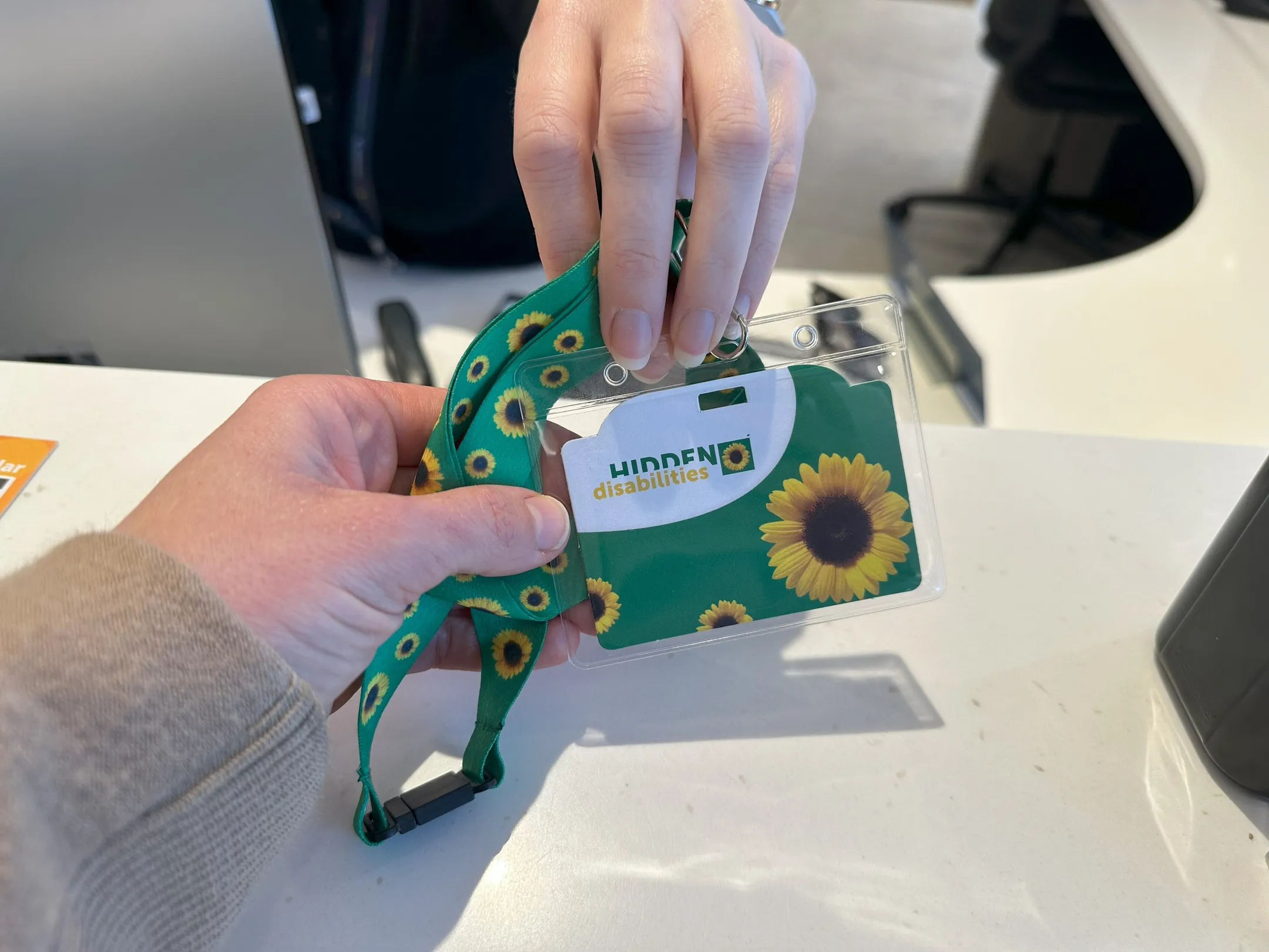 A person handing over a green sunflower lanyard at Sunshine Coast City Hall. The lanyard features a repeating pattern of bright yellow sunflowers, symbolizing hidden disabilities.