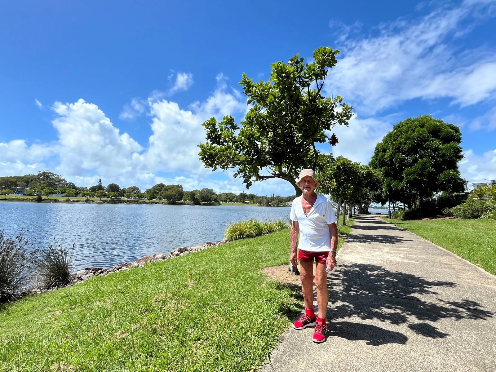 A senior man dressed in active wear standing in front of Lake Kawana on a sunny day.