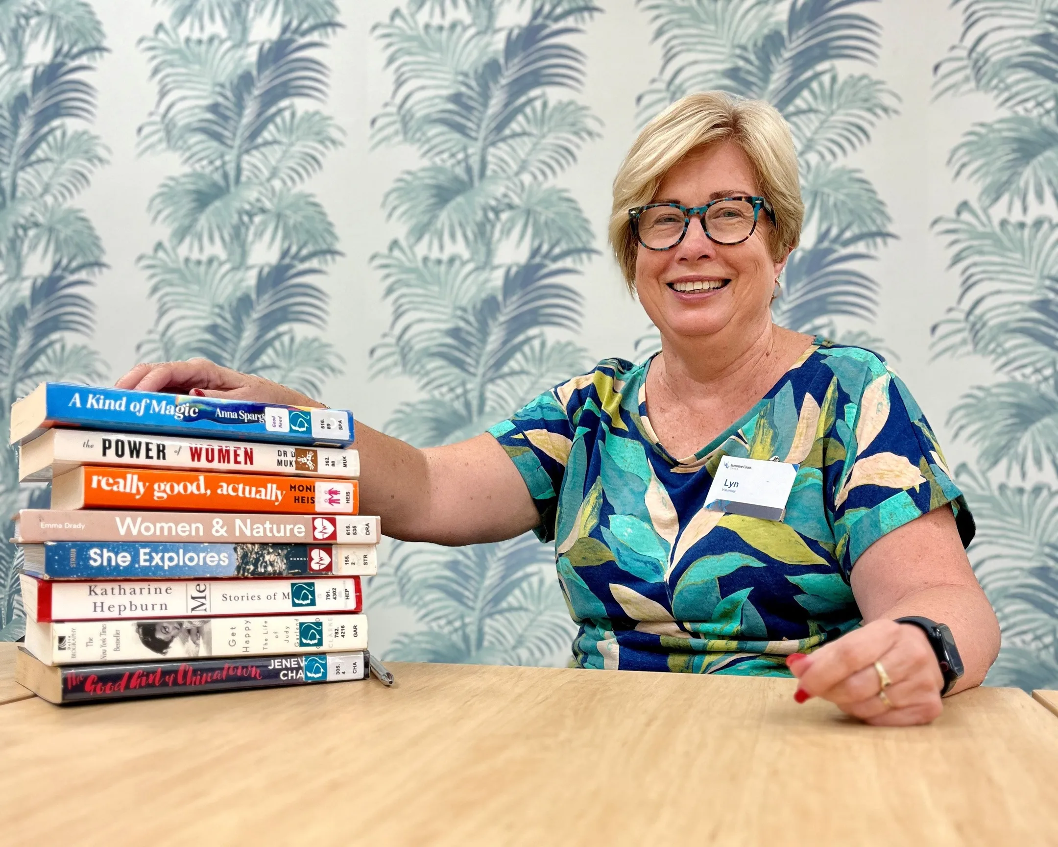 Volunteer Lyn Gavin sits with her hand on a stack of books.