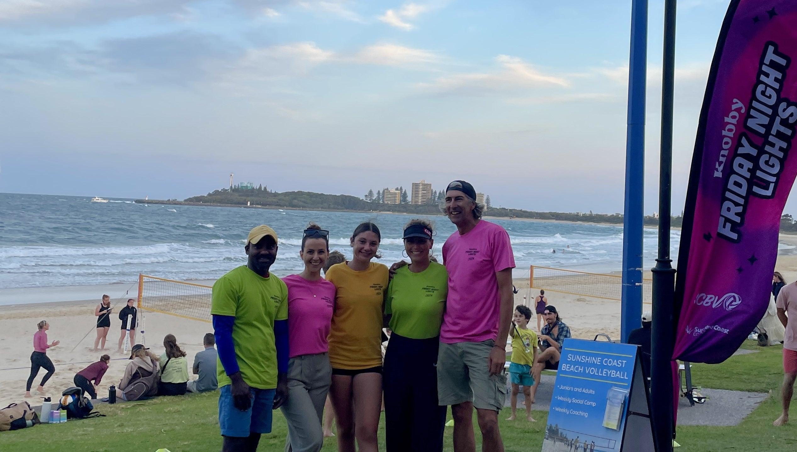 Game supporters posing together at Mooloolaba Beach, volleyball game happening behind them.