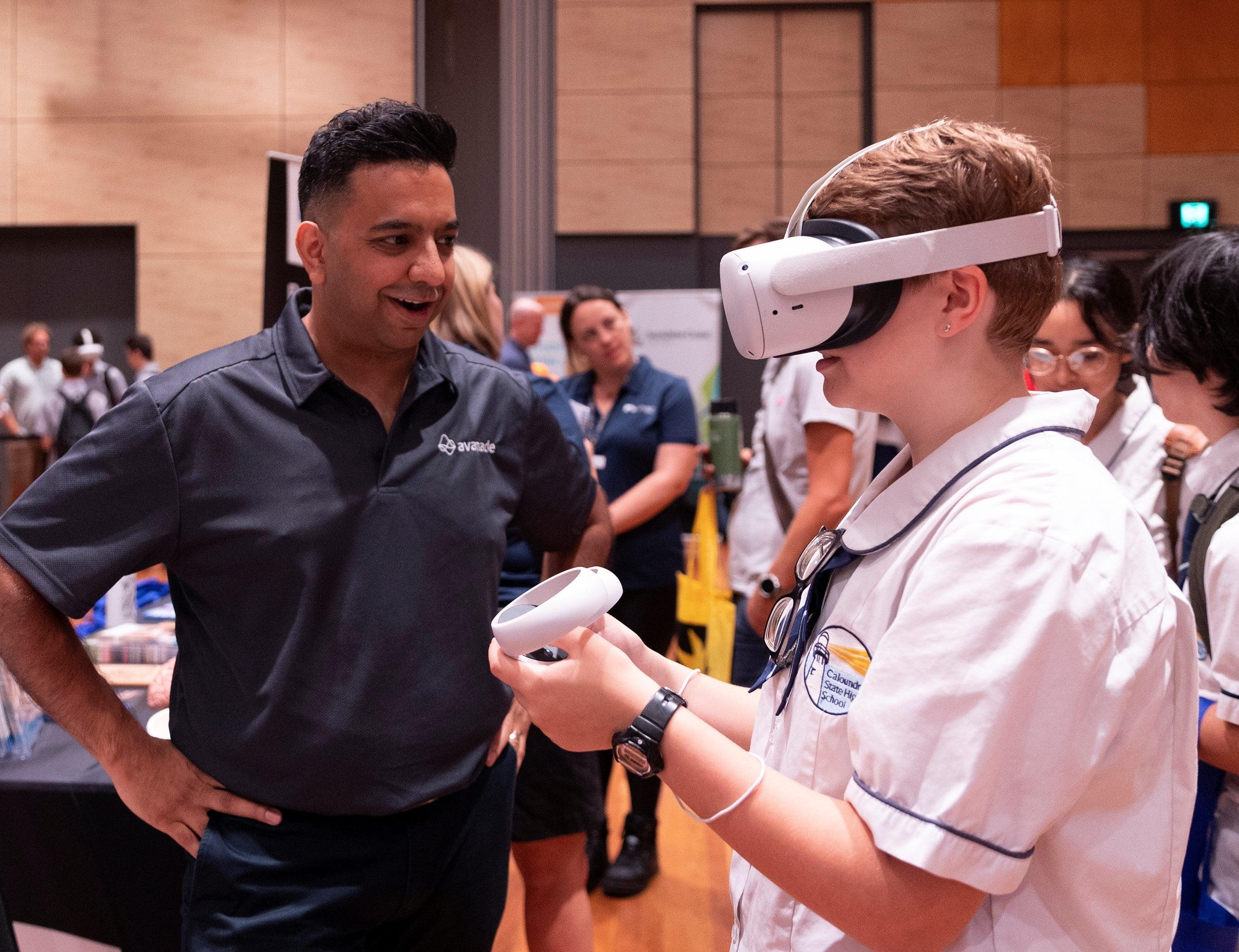 A student trying virtual reality equipment with a supplier next to the student providing guidance.