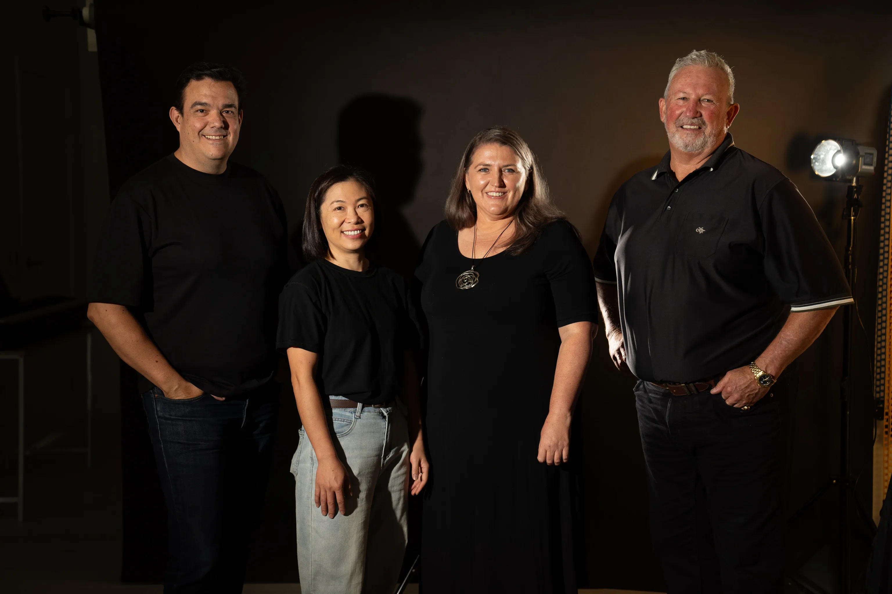 Four Shine a Light on Racism campaign patrons stand together wearing black with a golden light shining brightly behind them to help shine a light on racism.