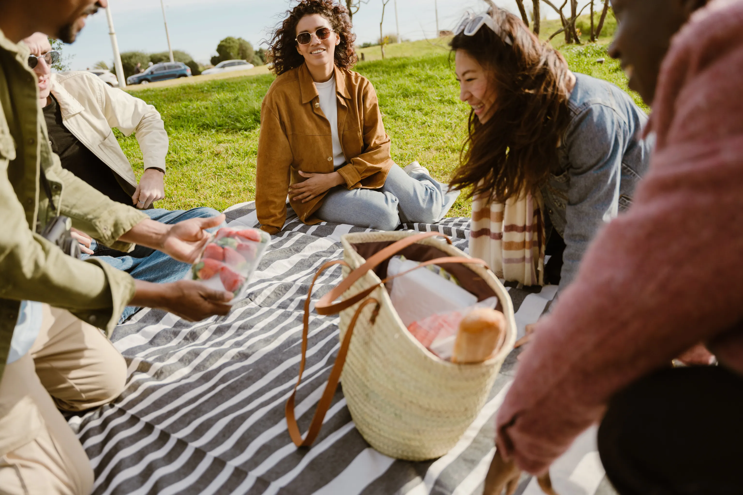 People sitting on a picnic blanket enjoying food and are smiling.