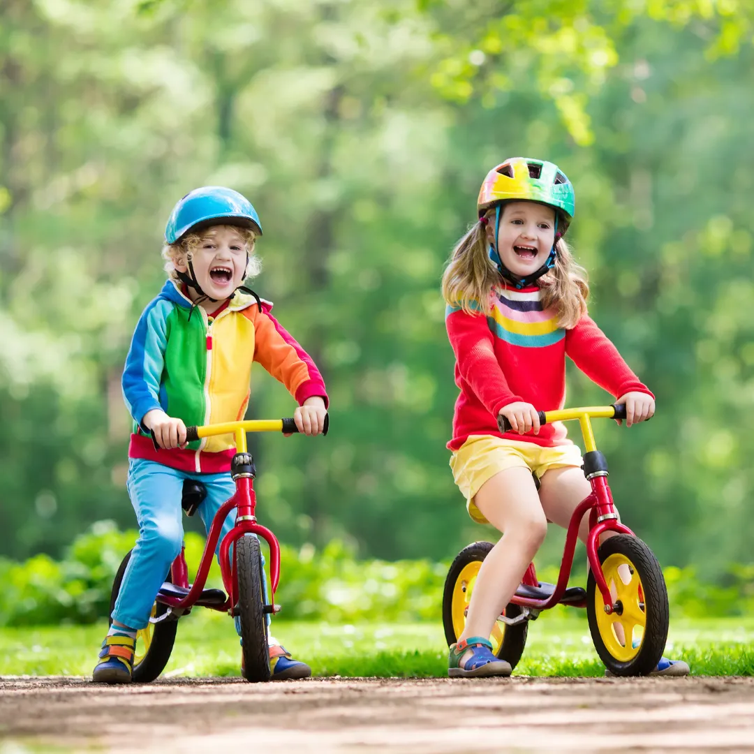 Young boy and girl on bicycles with helmets laughing.