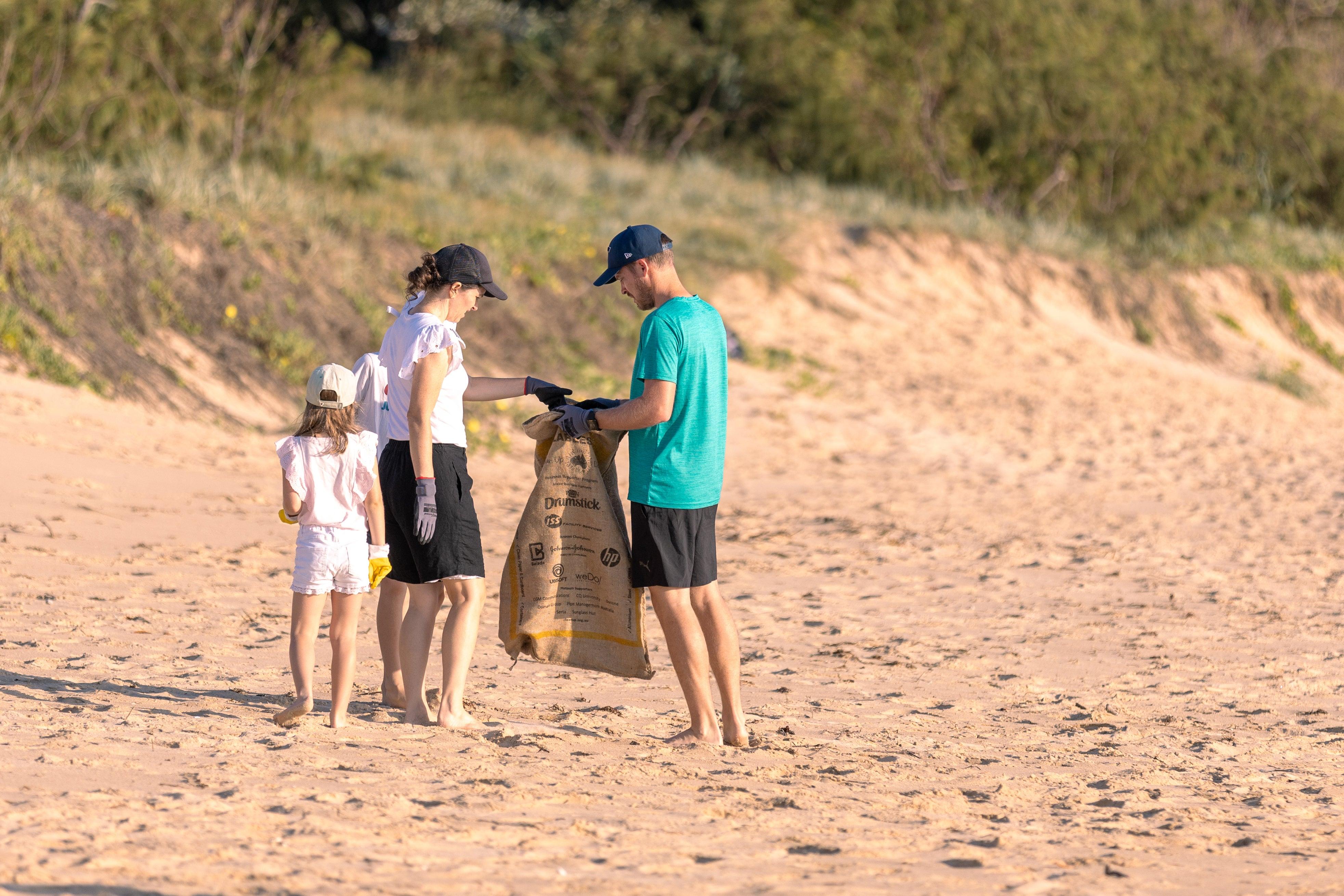 A group of people collecting rubbish on a sandy beach, working together to clean up the environment.