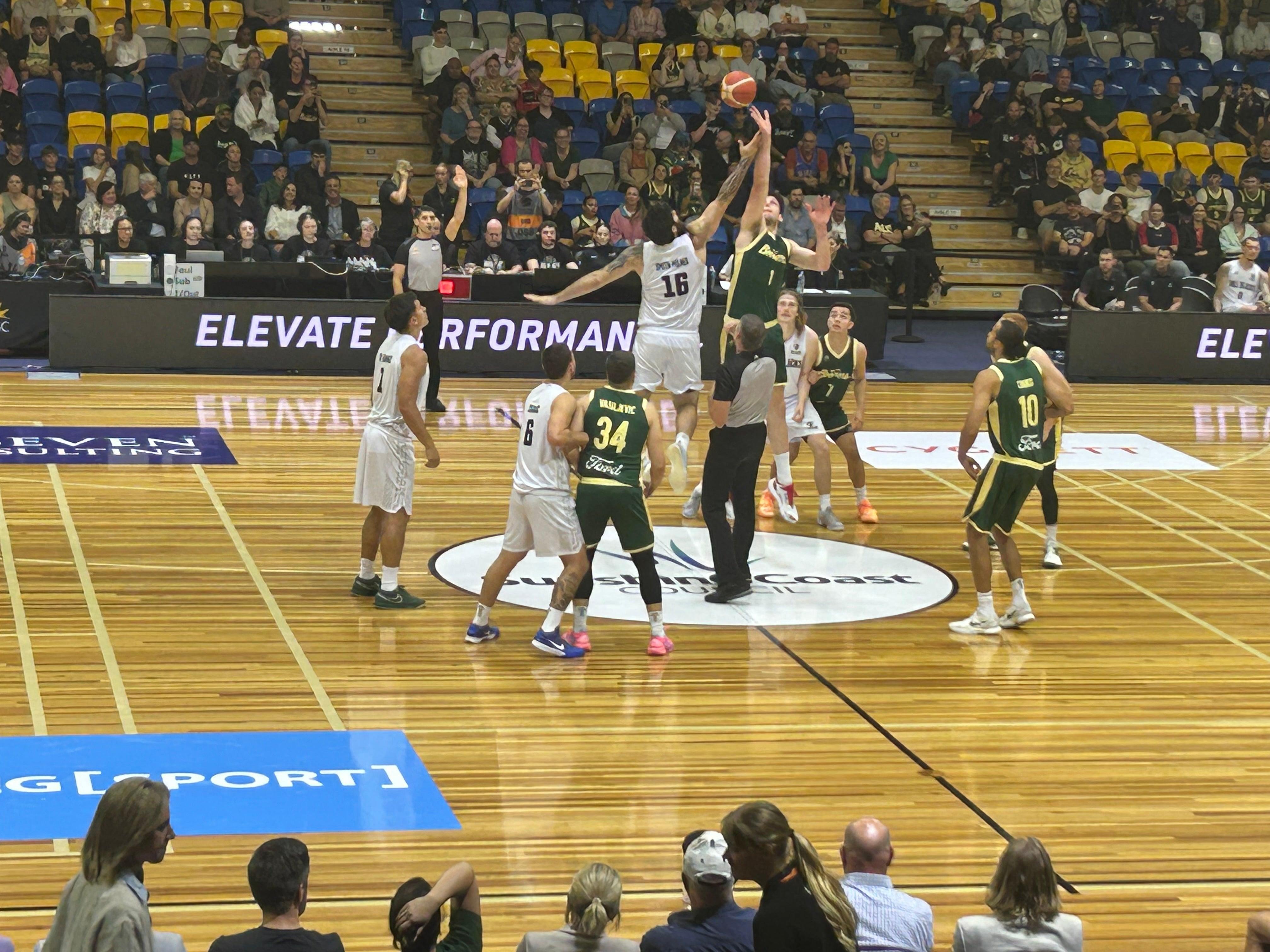 Basketball tip off to start the game with players jumping up for the ball.