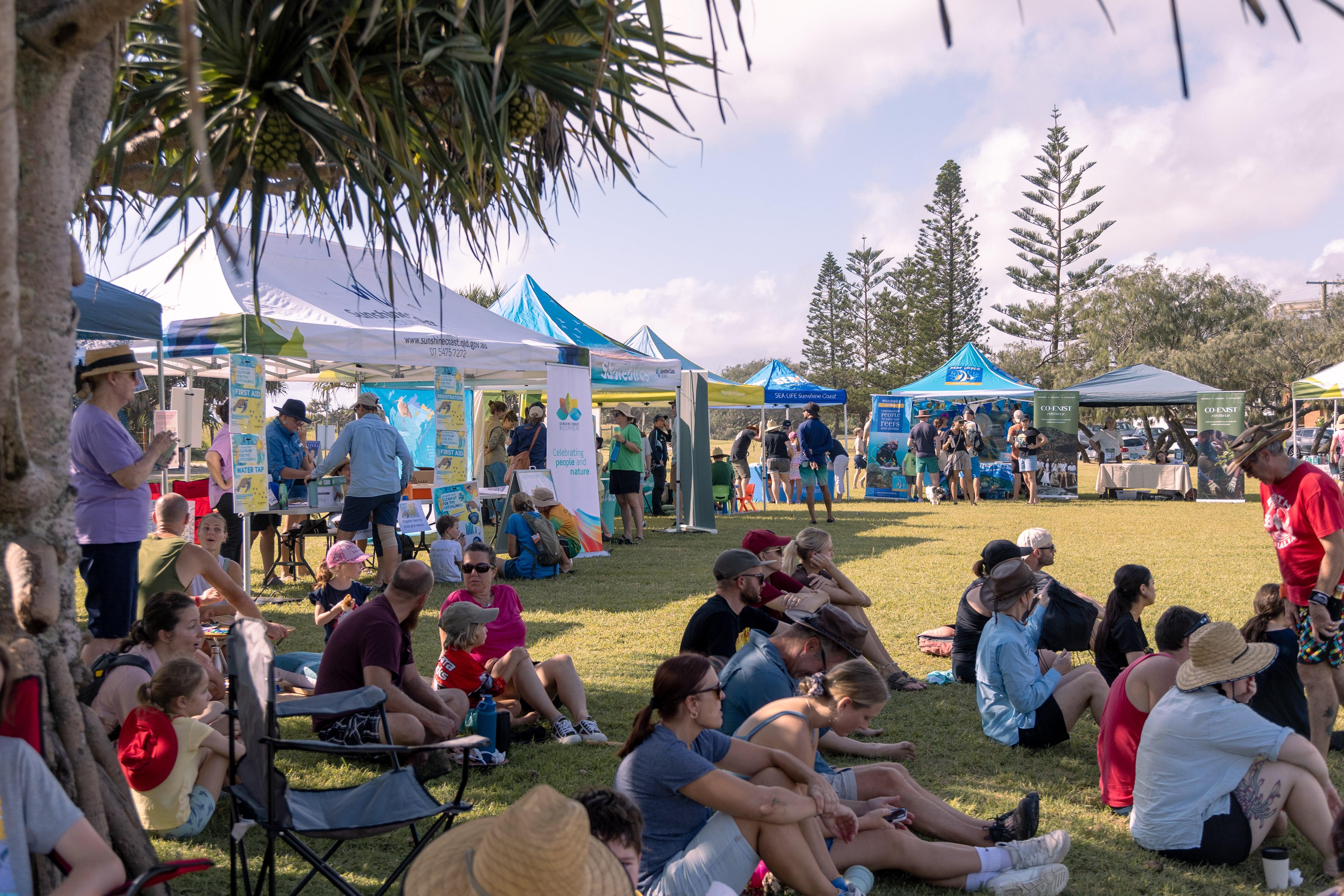 A large group of people sitting in the shade, watching presenters at a festival.