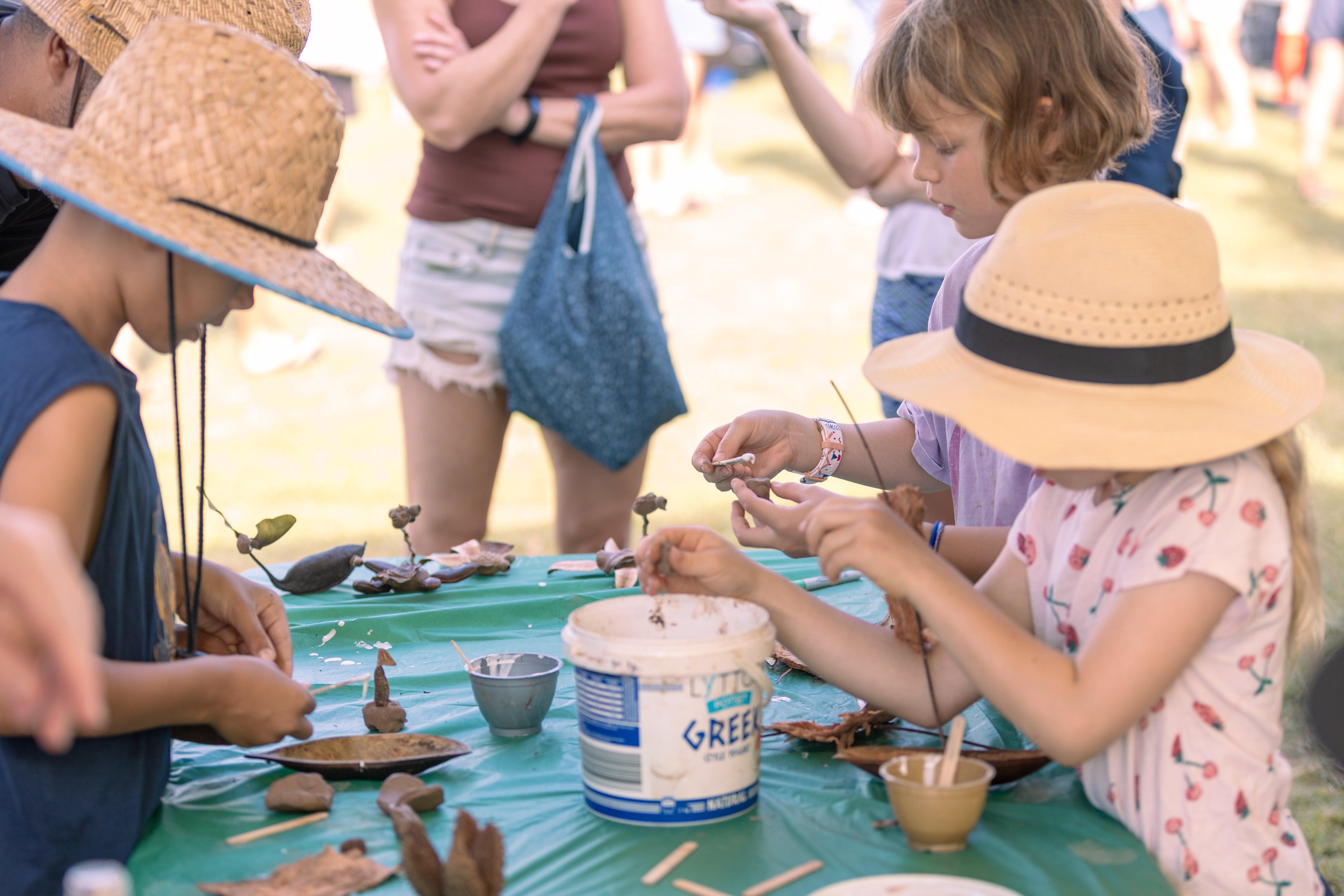 Children wearing hats, engaged in various art activities at a table, creating colorful artwork together.