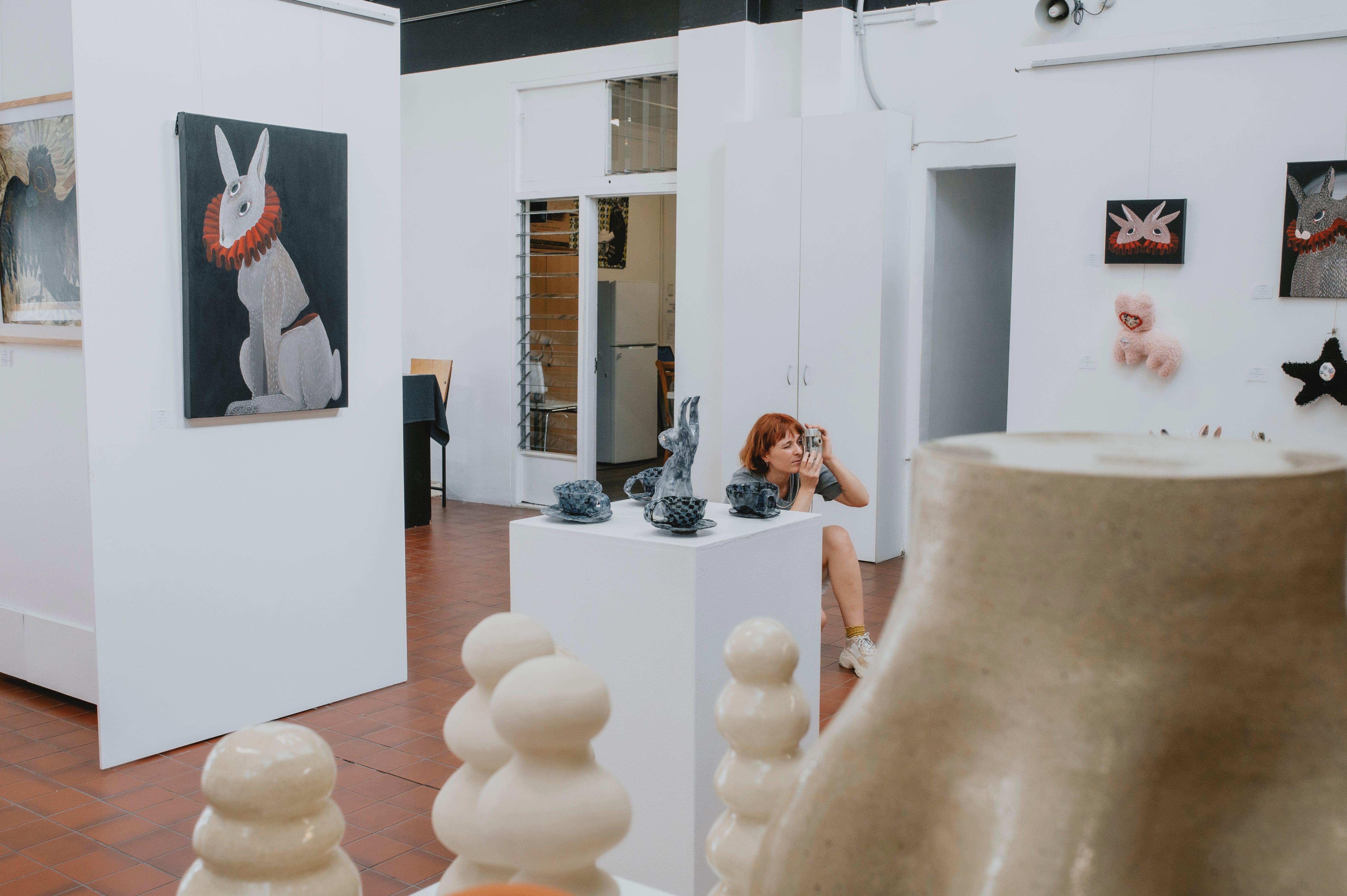 Lady taking a photo in art gallery with white walls - Image by Cooper Brady Photography