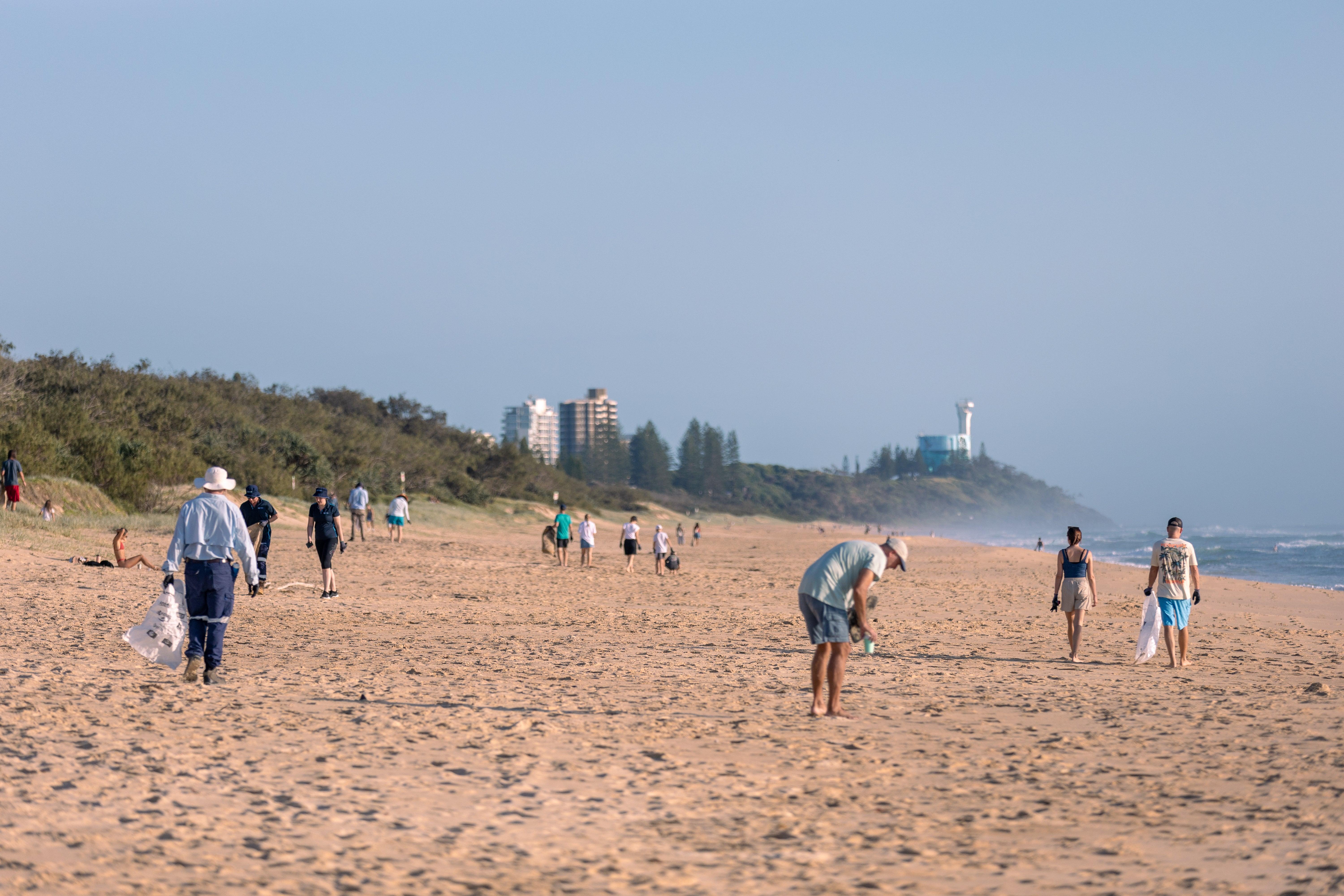 A group of people collecting rubbish on a sandy beach, working together to clean up the environment.