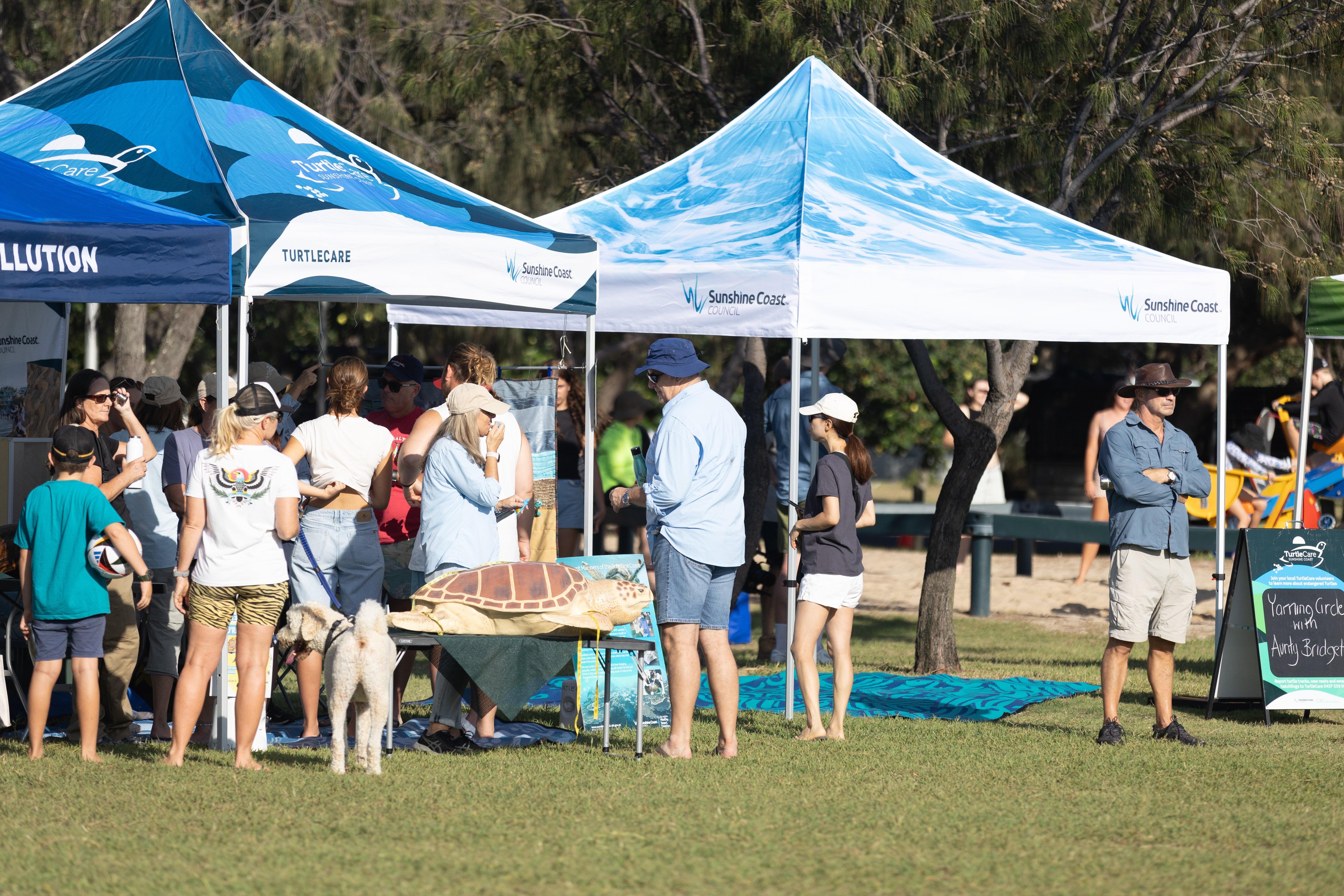 A group of people gathered around education stalls at the Clean up for the hatchlings thank you event.