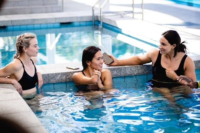 Three ladies in swimming pool of blue water, chatting and enjoying each others company